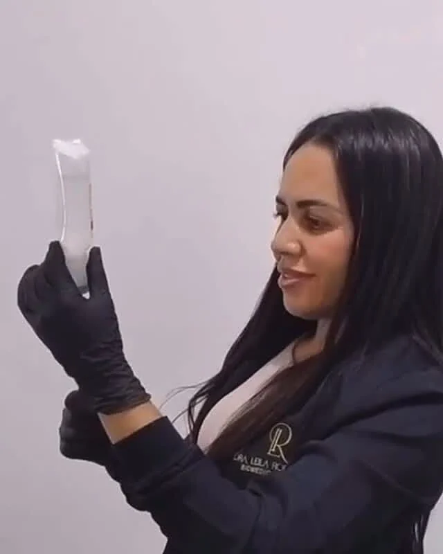 Dra. Leila Rodrigues de luvas pretas, sorrindo enquanto prepara um procedimento